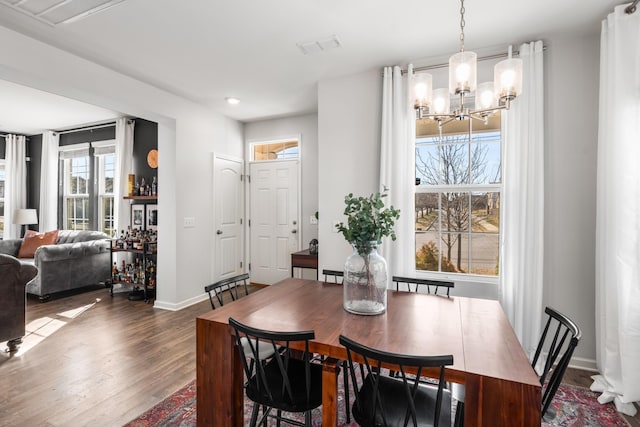 dining space with baseboards, wood finished floors, visible vents, and an inviting chandelier