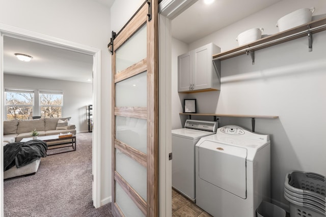 clothes washing area featuring a barn door, washing machine and dryer, carpet flooring, baseboards, and cabinet space