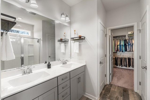 full bathroom with double vanity, wood finished floors, a stall shower, and a sink