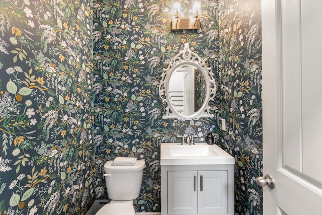 bathroom with toilet, wallpapered walls, and vanity