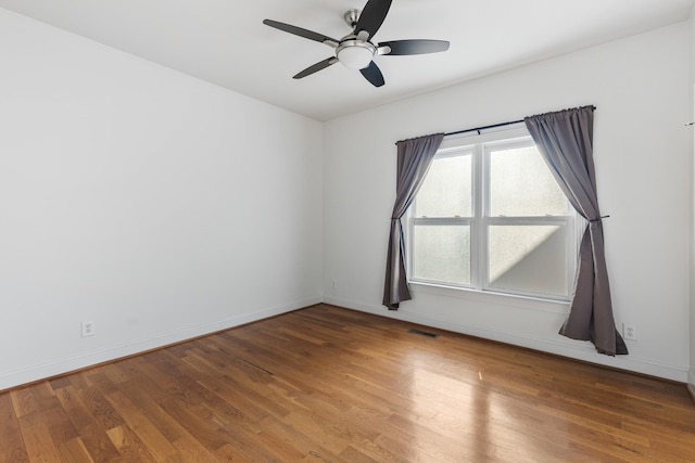 empty room with ceiling fan, wood finished floors, visible vents, and baseboards