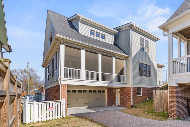 view of front of house with a sunroom, roof with shingles, an attached garage, fence, and brick siding