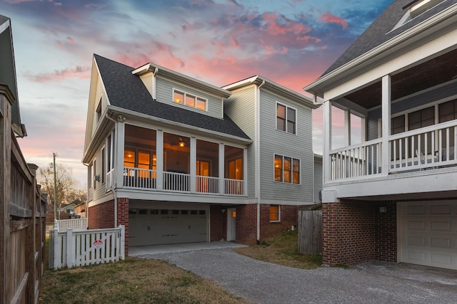 view of front of house with an attached garage, brick siding, fence, roof with shingles, and gravel driveway