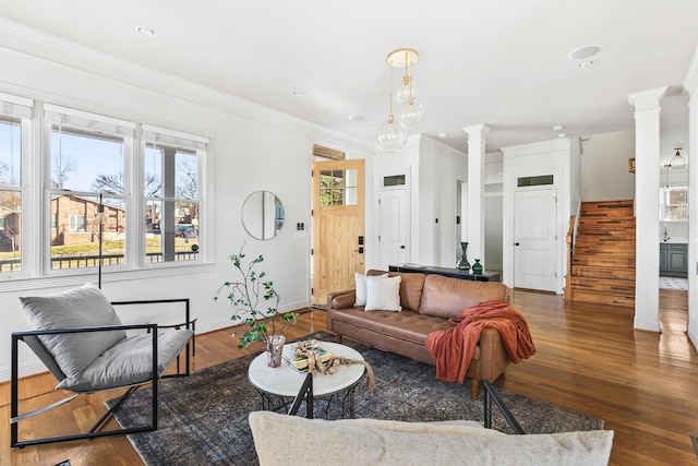 living room featuring stairs, crown molding, wood finished floors, and ornate columns