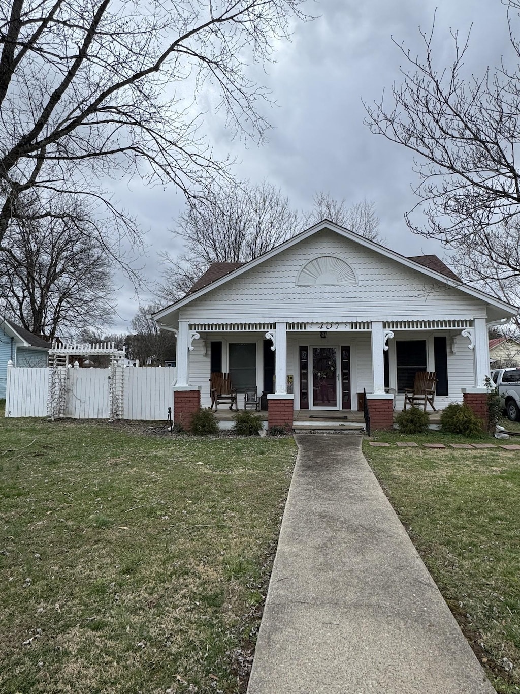 bungalow featuring a porch, a front yard, fence, and brick siding