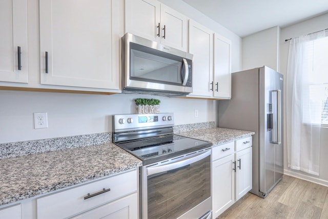 kitchen with white cabinets, light wood finished floors, stainless steel appliances, and light stone countertops