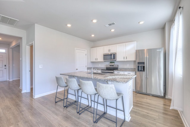 kitchen featuring a breakfast bar area, stainless steel appliances, visible vents, a sink, and light wood-type flooring