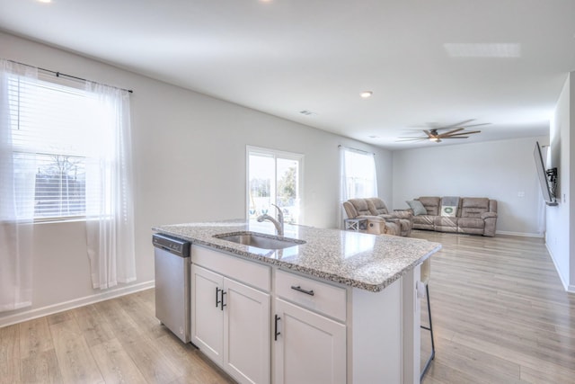 kitchen with light wood finished floors, white cabinets, a kitchen island with sink, a sink, and dishwasher