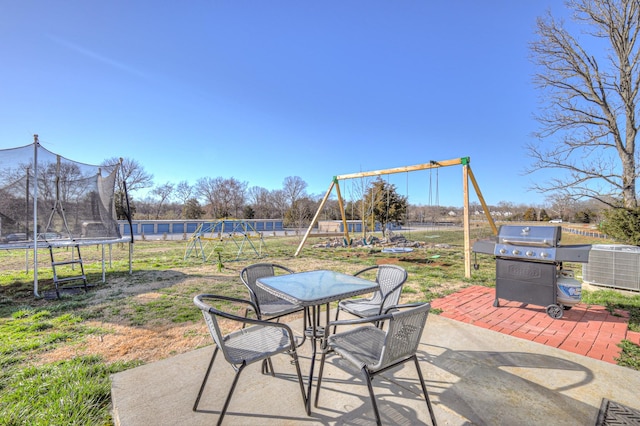 view of patio featuring playground community, a grill, fence, outdoor dining space, and a trampoline