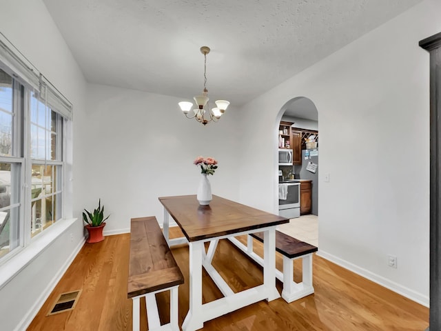 dining space featuring arched walkways, light wood finished floors, visible vents, and baseboards