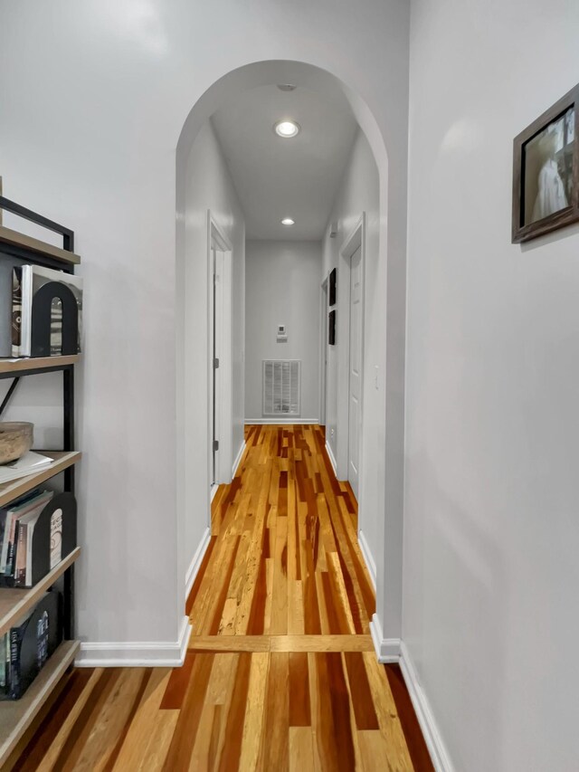 hall with arched walkways, light wood-type flooring, visible vents, and baseboards