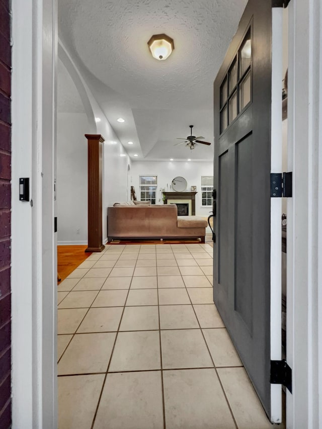 foyer featuring light tile patterned floors, arched walkways, ceiling fan, a textured ceiling, and a fireplace