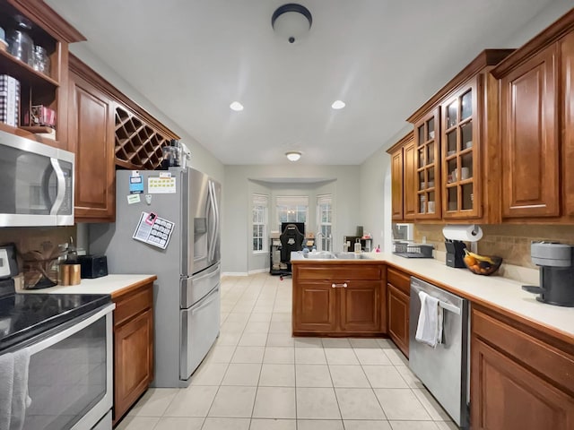 kitchen featuring light tile patterned flooring, light countertops, appliances with stainless steel finishes, backsplash, and brown cabinetry