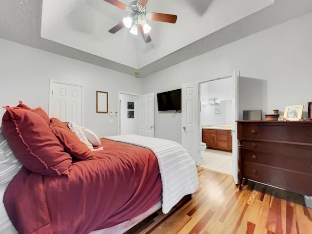 bedroom featuring a tray ceiling, vaulted ceiling, ceiling fan, ensuite bath, and light wood-type flooring