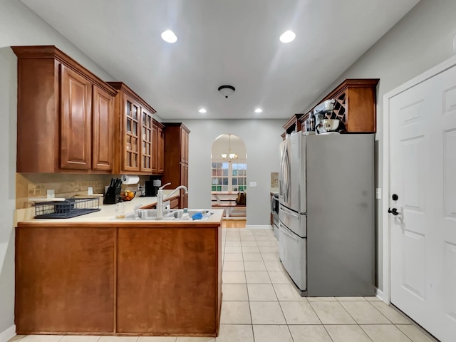 kitchen with arched walkways, light tile patterned floors, a peninsula, stainless steel refrigerator with ice dispenser, and glass insert cabinets