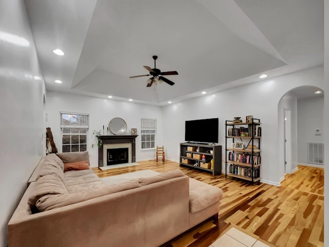 living room with arched walkways, recessed lighting, visible vents, light wood-type flooring, and a raised ceiling