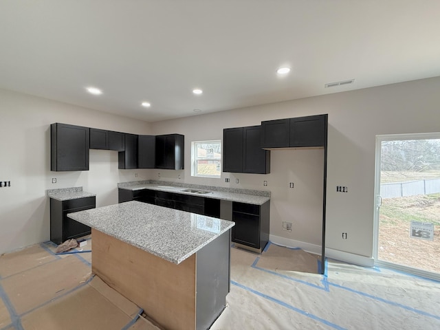 kitchen with dark cabinetry, light stone counters, visible vents, recessed lighting, and a center island