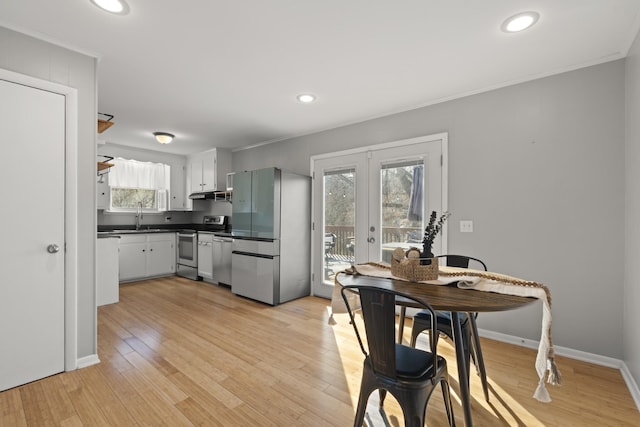 kitchen featuring stainless steel appliances, a sink, light wood-style floors, french doors, and dark countertops