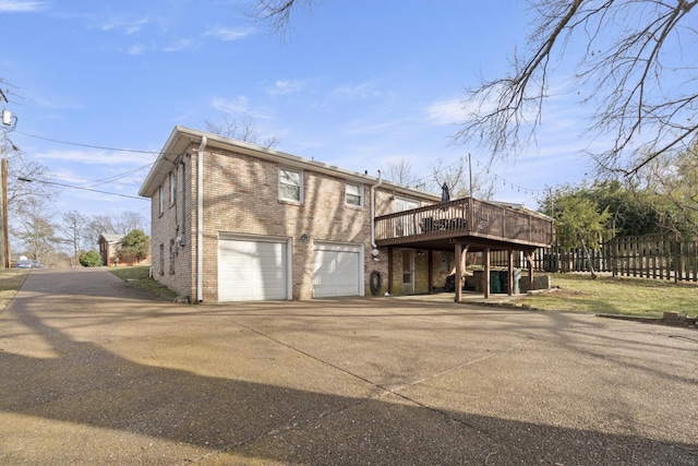 back of house featuring a garage, driveway, a deck, and brick siding