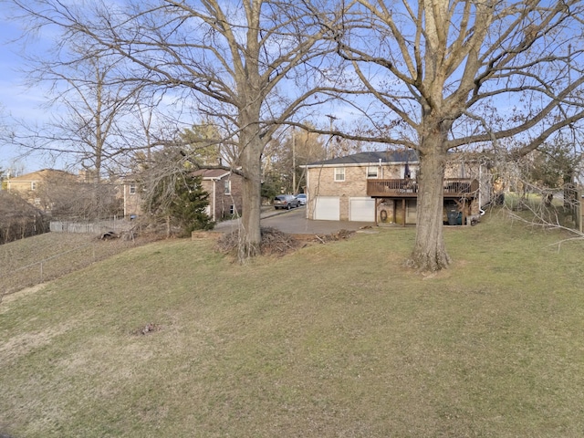 view of yard with driveway, an attached garage, and a wooden deck