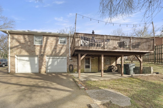 rear view of house featuring aphalt driveway, brick siding, a deck, and an attached garage