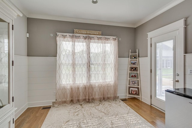 unfurnished dining area with a wainscoted wall, crown molding, visible vents, and wood finished floors