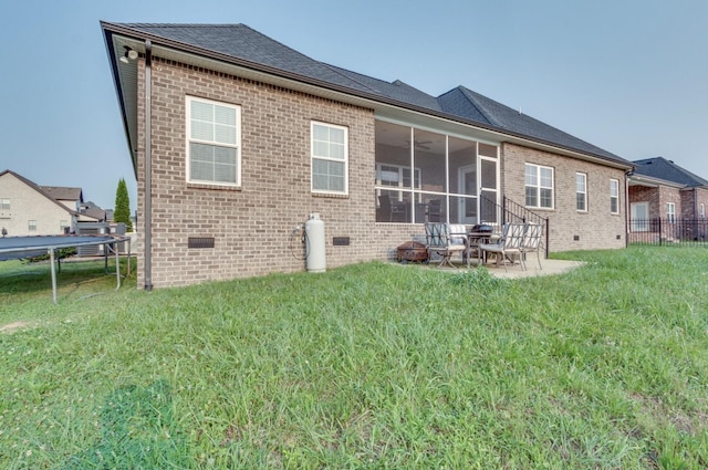 rear view of property with brick siding, a sunroom, a yard, crawl space, and a trampoline