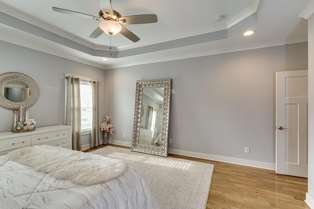 bedroom with a ceiling fan, a tray ceiling, light wood-style flooring, and baseboards