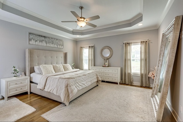 bedroom featuring a tray ceiling, multiple windows, ceiling fan, and wood finished floors