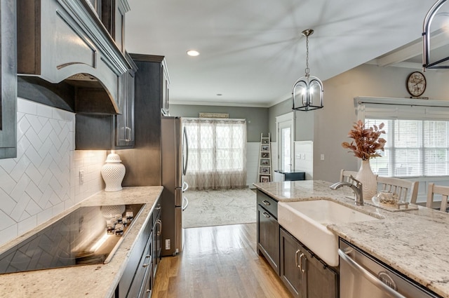 kitchen with custom range hood, appliances with stainless steel finishes, a sink, light stone countertops, and light wood-type flooring