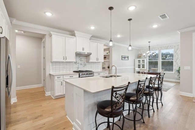 kitchen with under cabinet range hood, a breakfast bar, a sink, appliances with stainless steel finishes, and crown molding