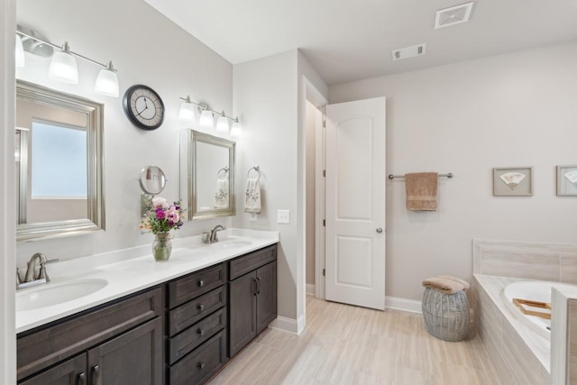 bathroom with tiled bath, visible vents, and a sink