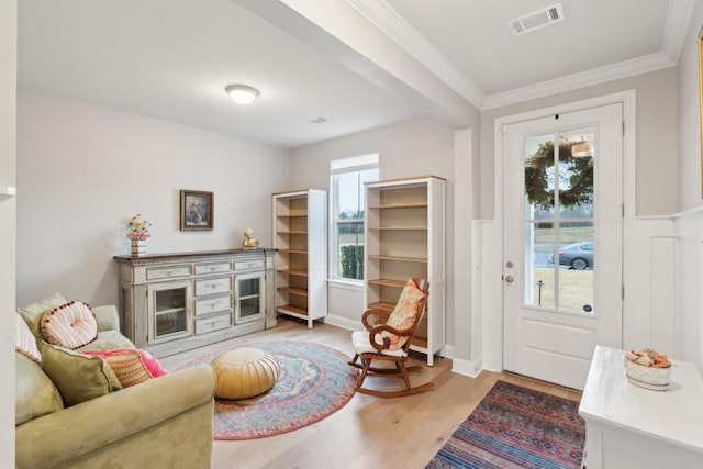 living area featuring a healthy amount of sunlight, light wood-type flooring, visible vents, and crown molding