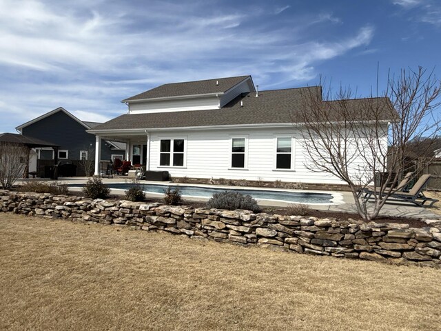 back of property featuring a yard, roof with shingles, a patio area, and an outdoor pool