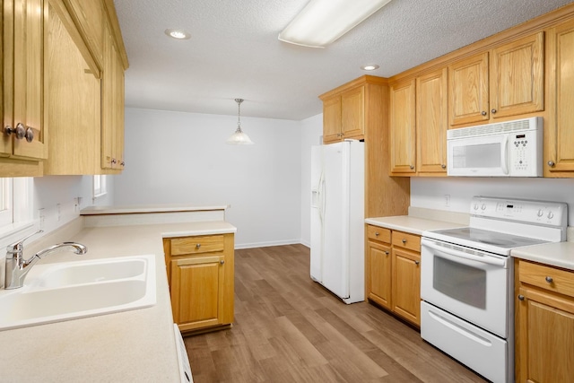 kitchen featuring white appliances, wood finished floors, light countertops, a sink, and recessed lighting