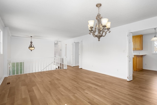 unfurnished dining area with light wood-style floors, crown molding, and an inviting chandelier