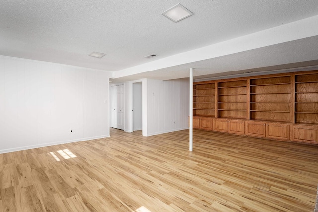 finished below grade area featuring light wood-style floors, built in shelves, baseboards, and a textured ceiling