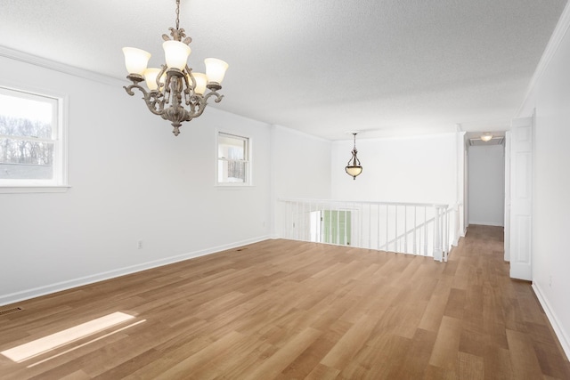 spare room featuring a chandelier, light wood finished floors, ornamental molding, and baseboards