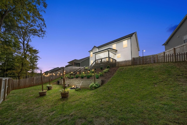 back of property at dusk with a garden, a lawn, and a fenced backyard