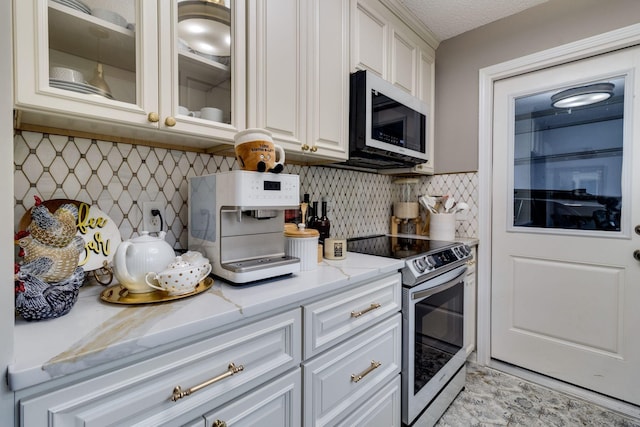 kitchen featuring white cabinets, white microwave, glass insert cabinets, light stone counters, and stainless steel electric range