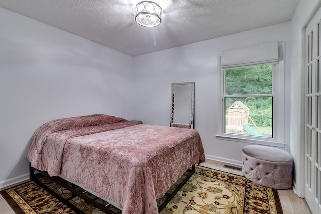 bedroom with light wood-type flooring, visible vents, a textured ceiling, and baseboards