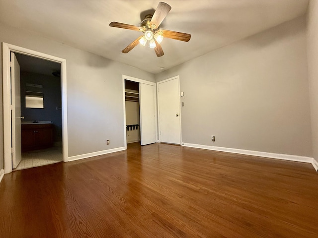 unfurnished bedroom with ensuite bath, a closet, baseboards, and dark wood-type flooring