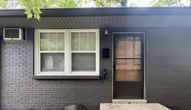 entrance to property featuring an AC wall unit and brick siding