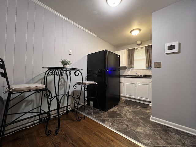 kitchen featuring dark wood-style floors, dark countertops, freestanding refrigerator, white cabinetry, and a sink