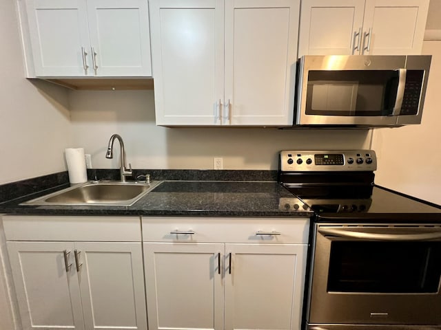 kitchen featuring dark stone counters, stainless steel appliances, a sink, and white cabinets