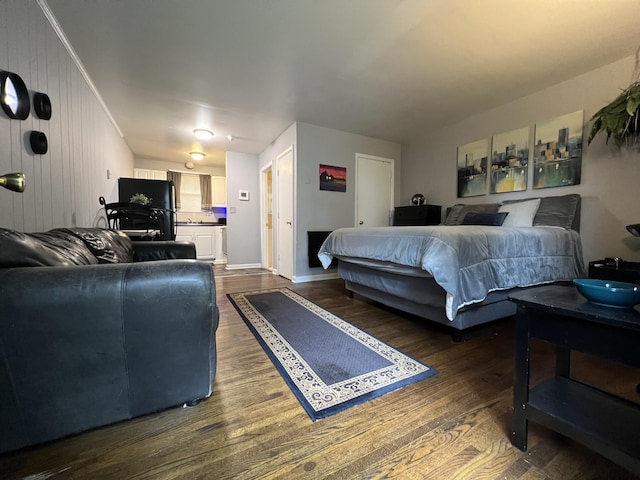 bedroom with freestanding refrigerator, dark wood finished floors, and baseboards