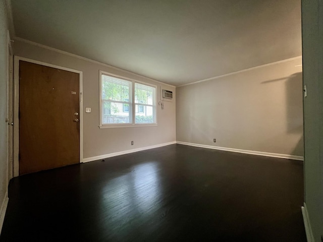 spare room featuring crown molding, dark wood-type flooring, a wall unit AC, and baseboards