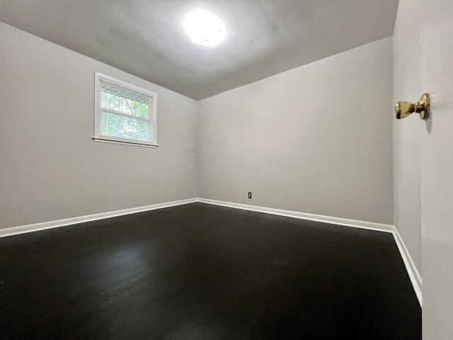 spare room featuring vaulted ceiling, dark wood finished floors, and baseboards