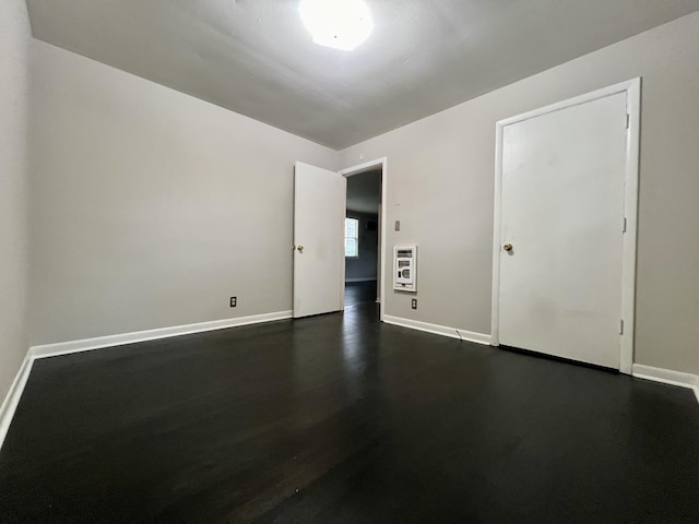 spare room featuring baseboards, dark wood-style flooring, and heating unit