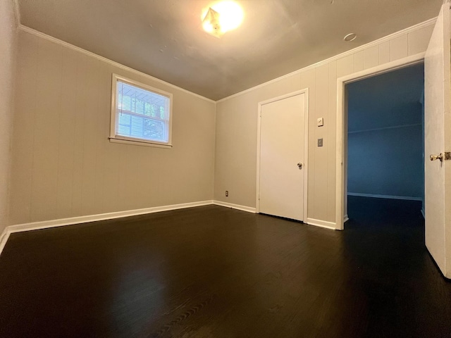 empty room with dark wood-style floors, baseboards, and ornamental molding